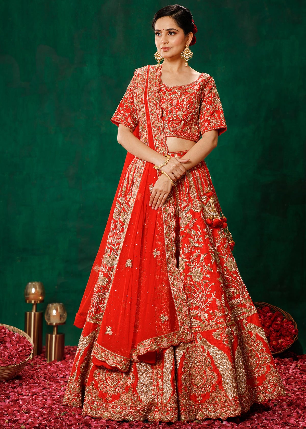 Woman in a red embroidered traditional outfit standing on red petals with a green background