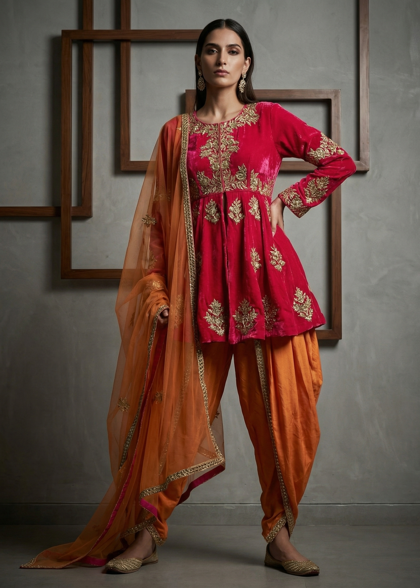 Woman wearing a red and orange traditional outfit with gold embroidery against a gray background.