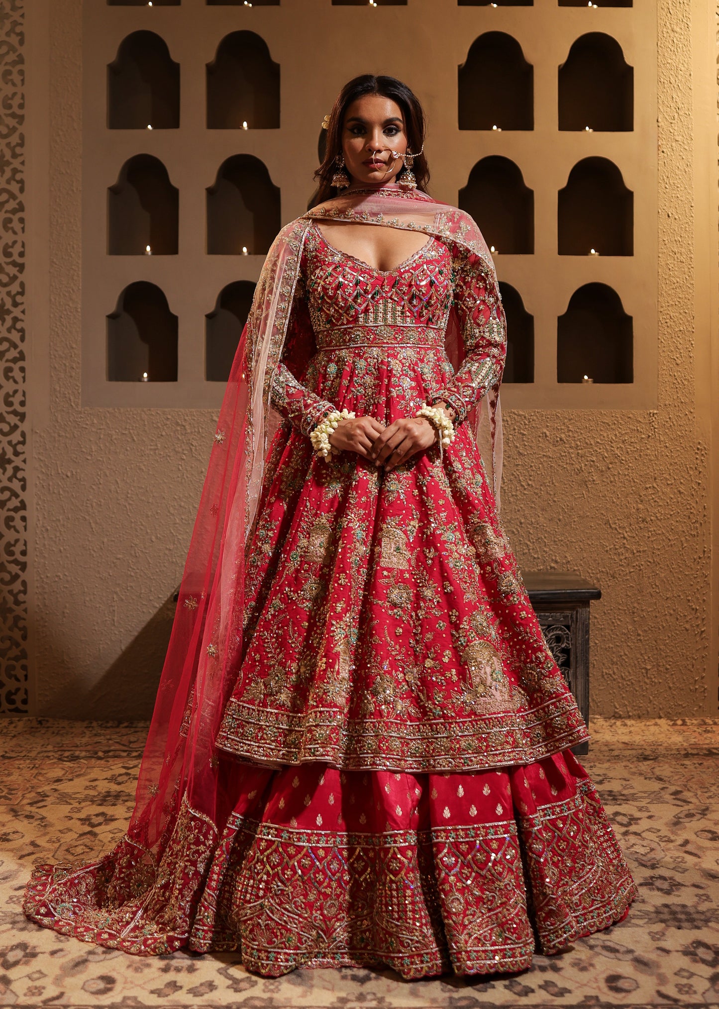 Woman in a red and gold traditional outfit standing against an ornate wall.