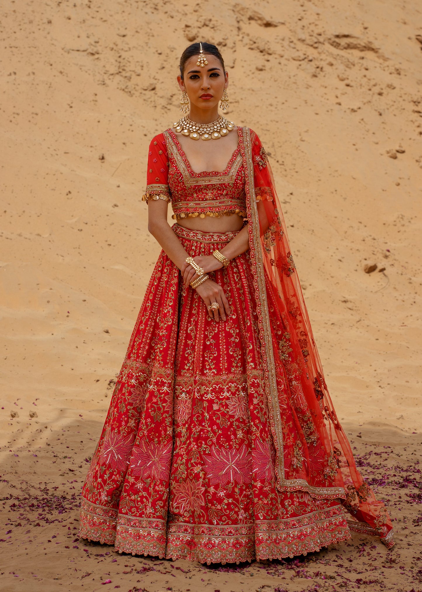 Woman in a traditional red embroidered outfit standing against a desert backdrop