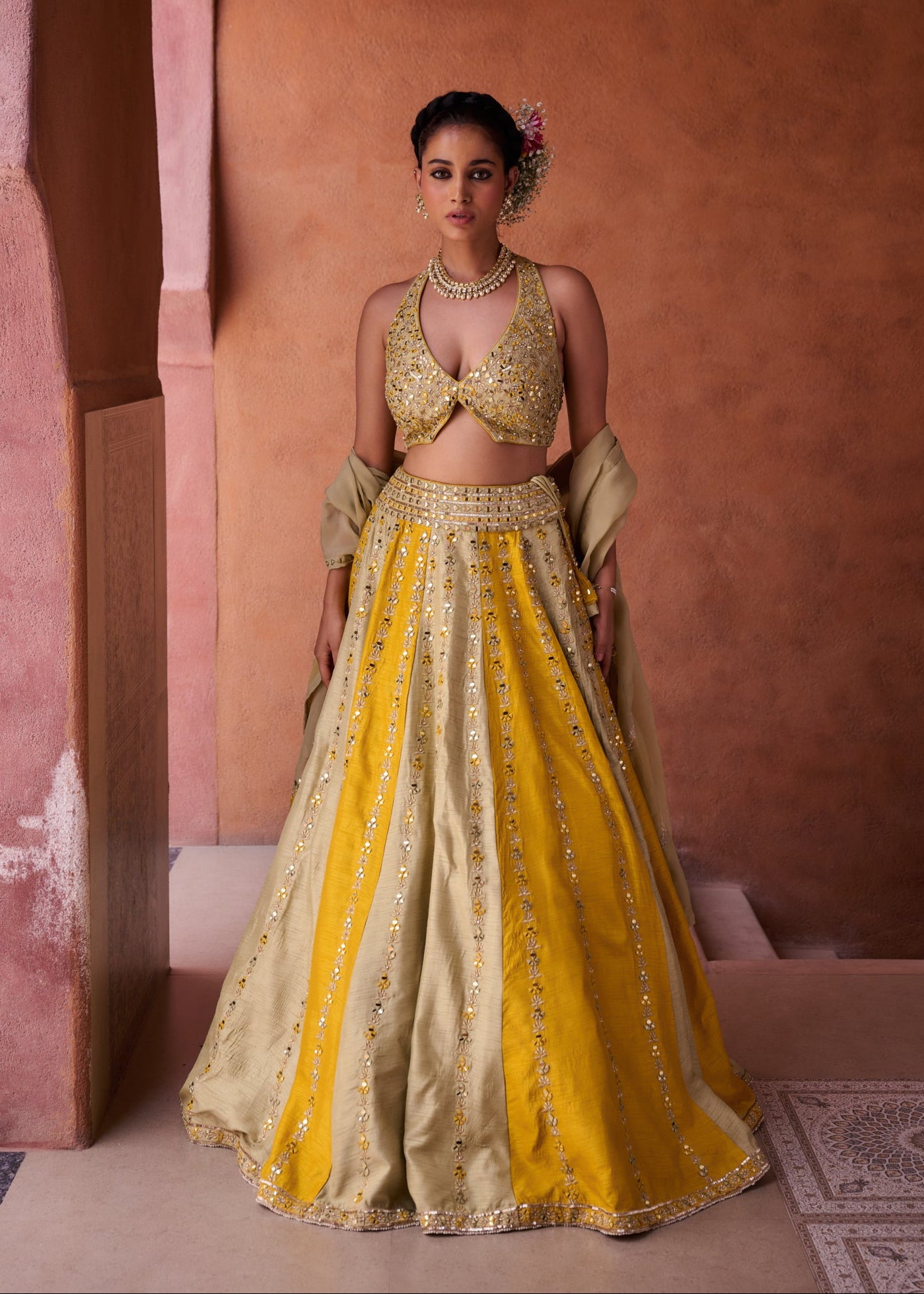 Woman in a yellow and gold traditional outfit standing against a warm-toned wall.