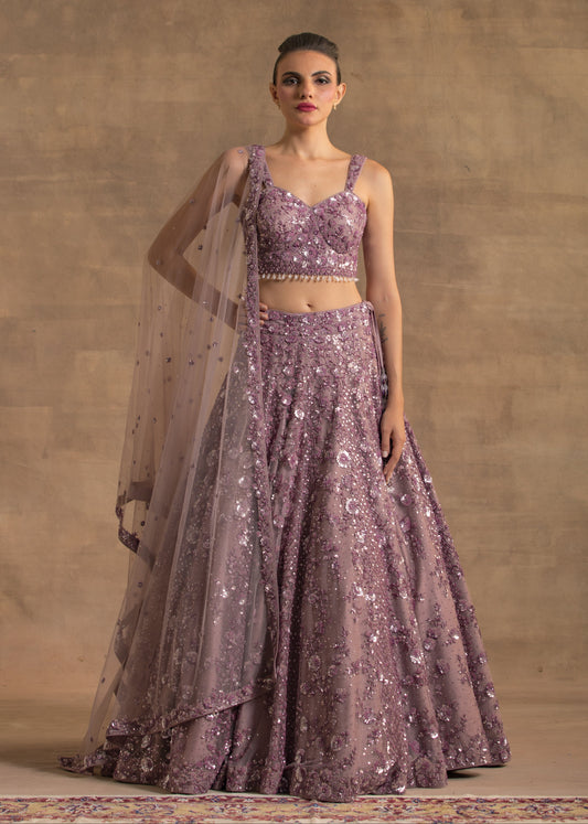 Woman wearing a purple embroidered outfit with a sheer dupatta against a beige background