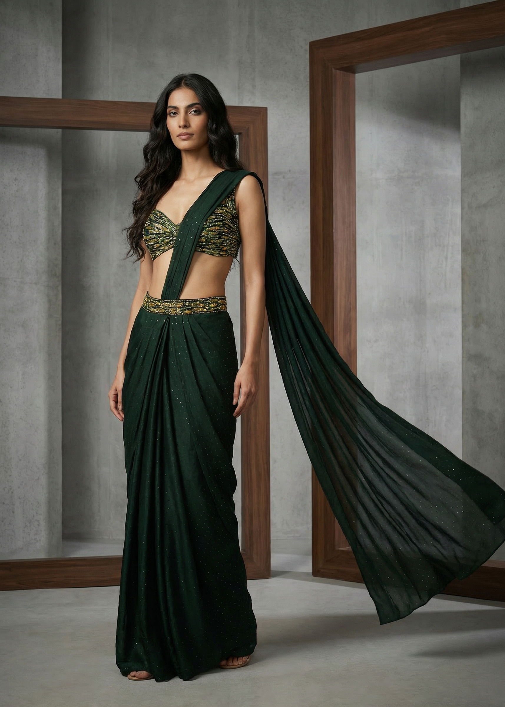 Woman wearing a dark green saree with a matching blouse in a minimalistic setting.