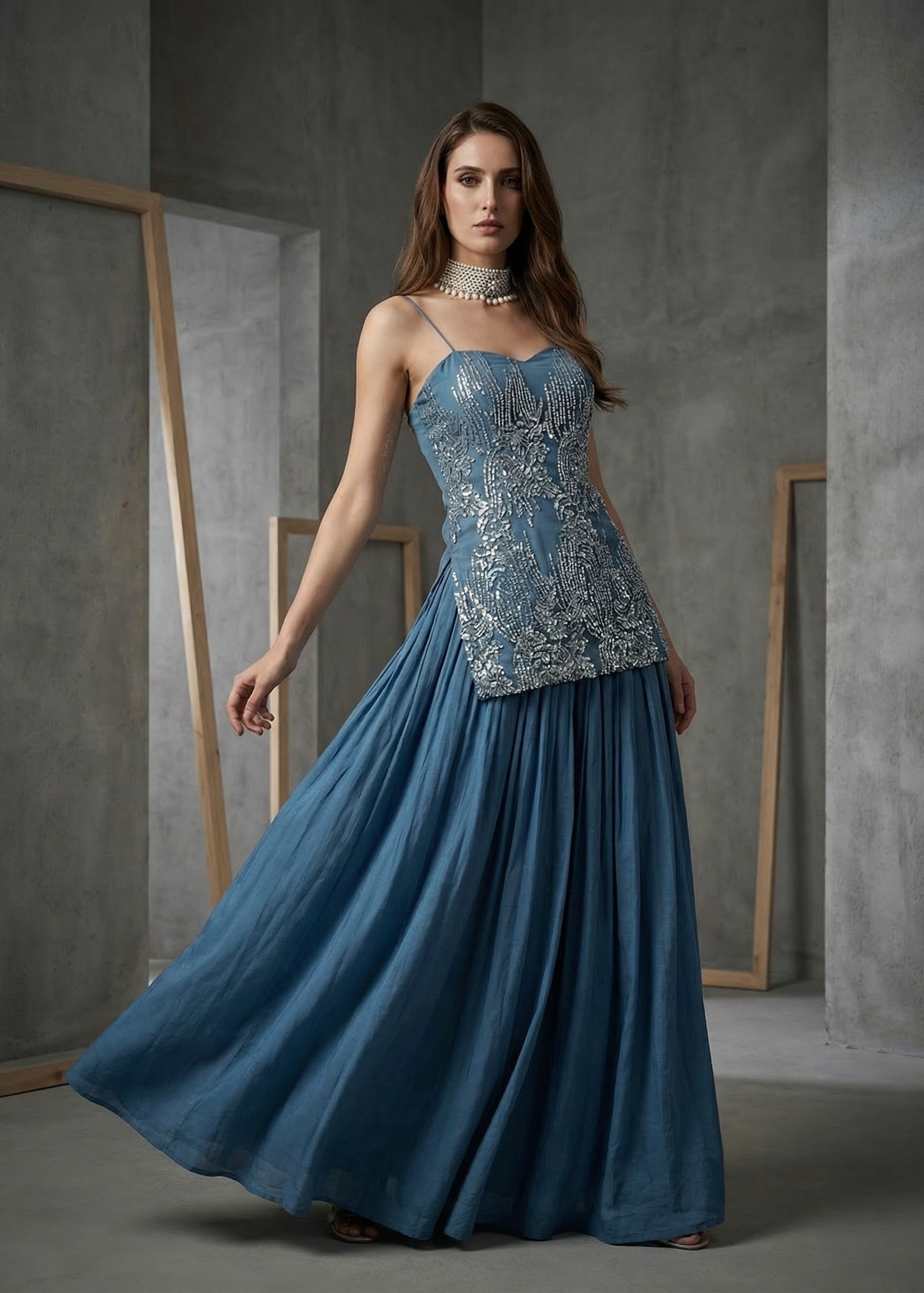 Woman wearing a blue evening gown with intricate detailing in a gray studio setting
