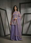 Woman wearing a traditional outfit with a purple top and skirt in a minimalistic setting.