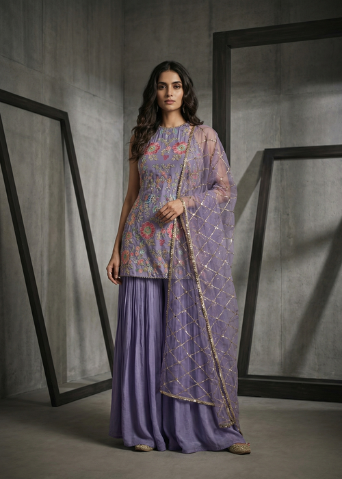 Woman wearing a traditional outfit with a purple top and skirt in a minimalistic setting.