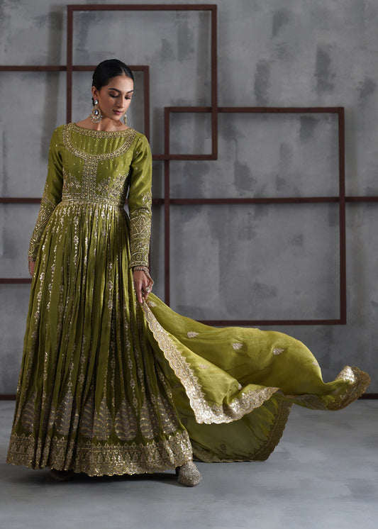 Woman in a green and gold traditional outfit with a flowing skirt against a gray wall.