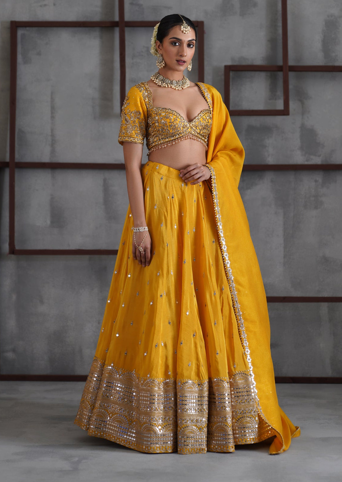Woman in a yellow traditional outfit standing against a gray textured wall.