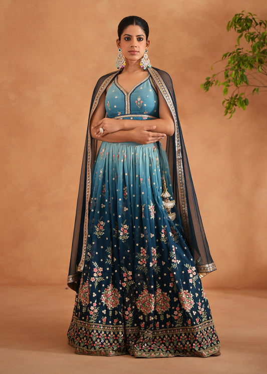 Woman wearing a traditional blue and black embroidered outfit against a beige background