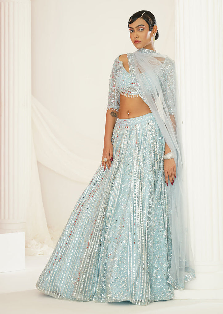 Woman in a light blue traditional outfit standing in a classical setting with columns.