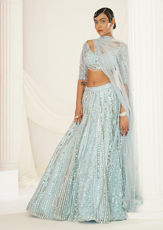 Woman in a light blue traditional outfit standing in a classical setting with columns.