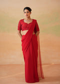 Woman wearing a red saree with a matching blouse against a beige background