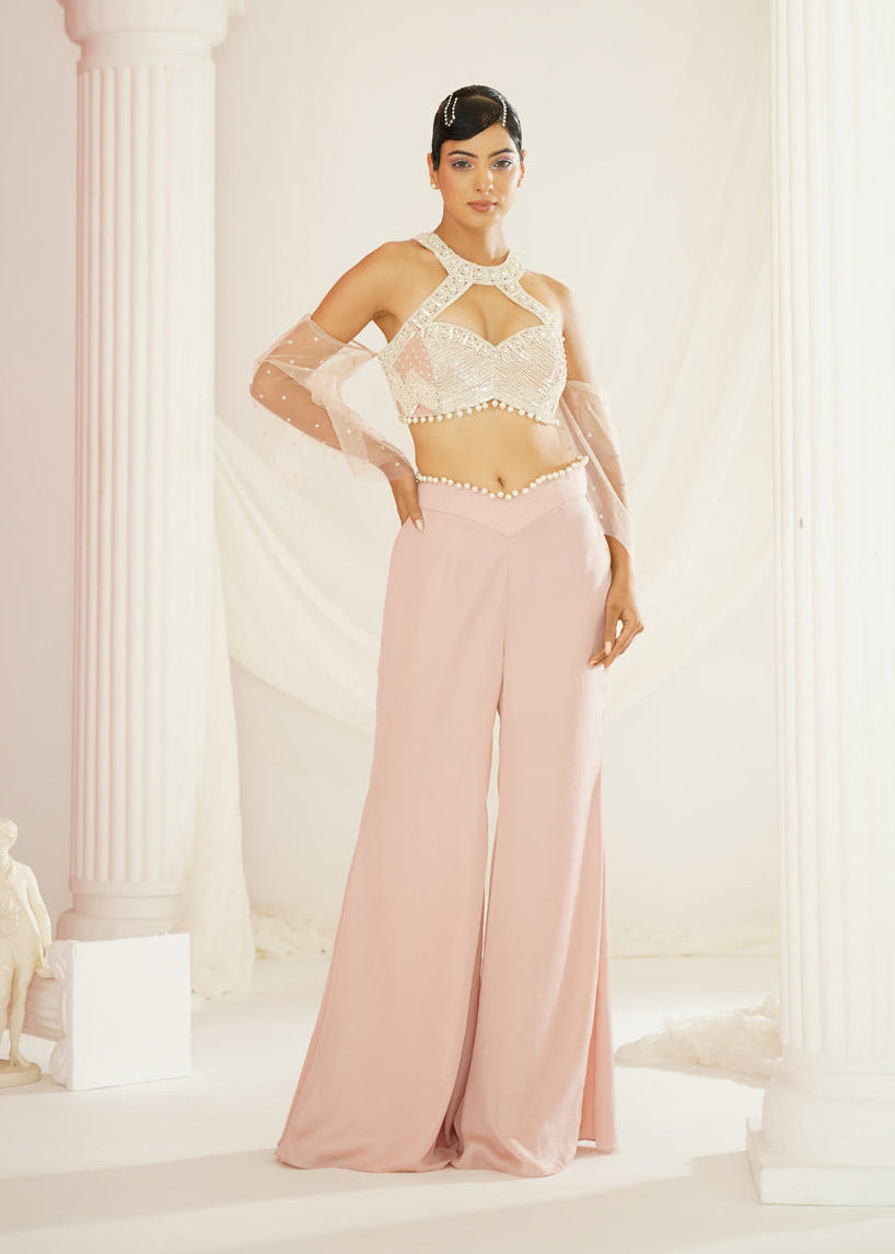 Woman in a white top and pink pants standing in a classical setting with columns.