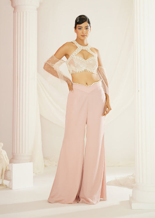 Woman in a white top and pink pants standing in a classical setting with columns.