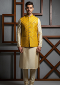 Man wearing a yellow Nehru jacket over a cream kurta against a gray wall with wooden decorative elements.
