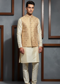 Man wearing a traditional cream kurta with an embroidered vest against a gray wall.