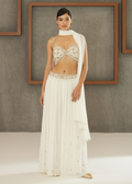 Woman wearing a white lace top and long white skirt against a gray wall with wooden frames.