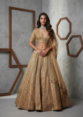 Woman in a gold traditional outfit standing against a gray wall with geometric wooden frames.