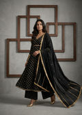 Woman in a black traditional outfit with gold details standing against a gray wall with wooden frames.