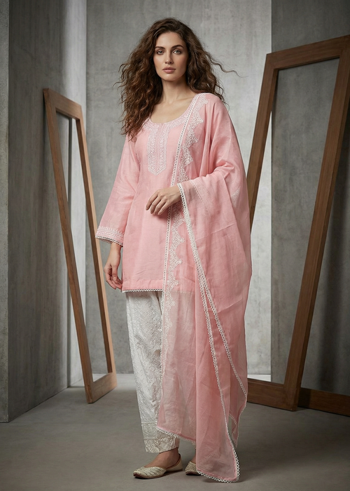 Woman wearing a pink traditional outfit with white lace in a minimalistic setting.