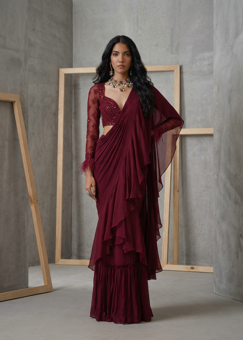 Woman wearing a burgundy saree with a matching blouse against a gray background