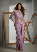Woman wearing a lavender outfit with a sheer cape against a gray background