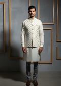 Man wearing a traditional kurta with a patterned jacket against a gray wall.