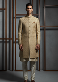 Man wearing a traditional beige sherwani with white pants against a gray background