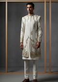 Man wearing a traditional embroidered sherwani against a gray background