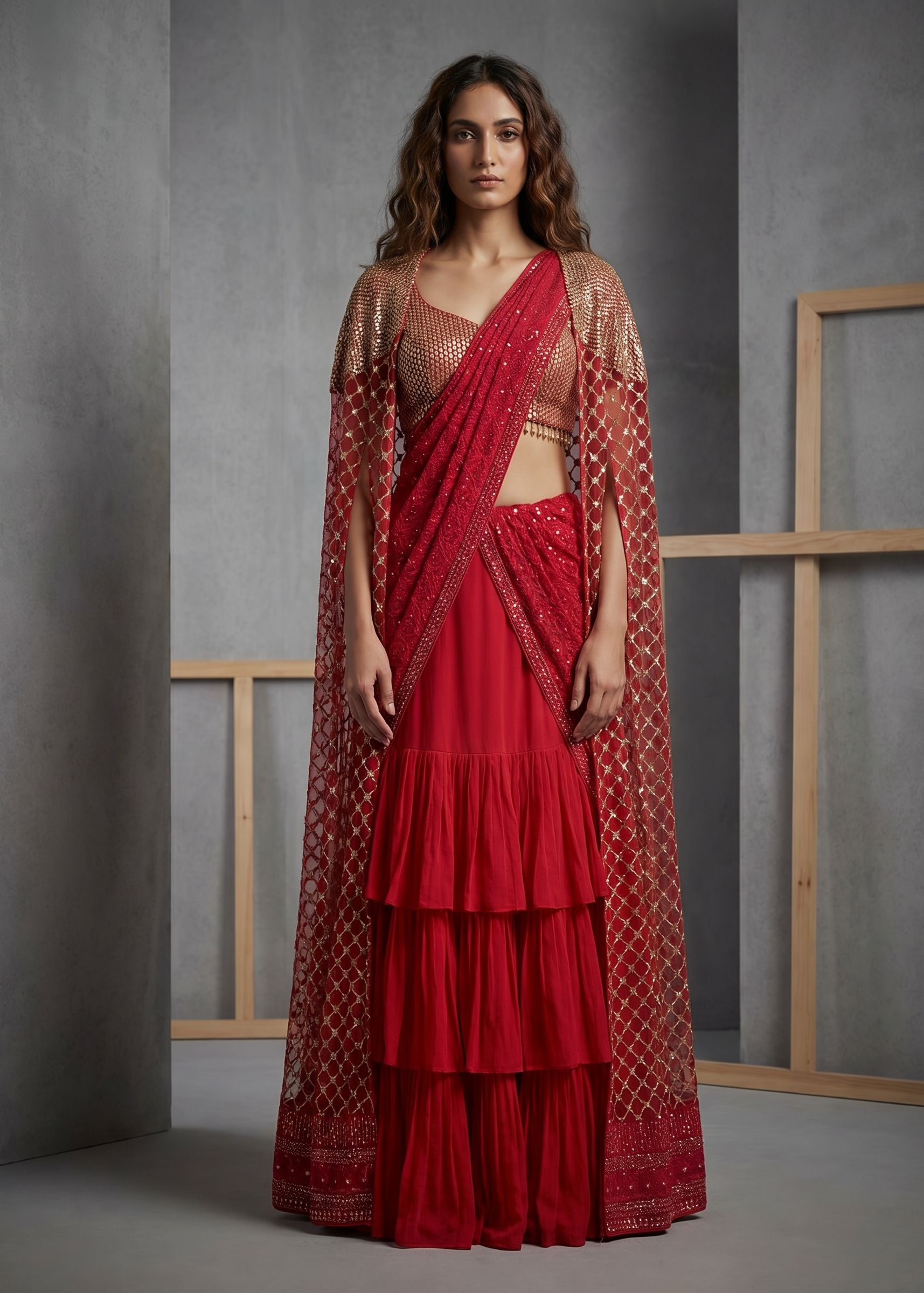 Woman wearing a red saree with gold patterns against a gray background
