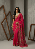 Woman wearing a pink saree with gold embroidery against a gray background