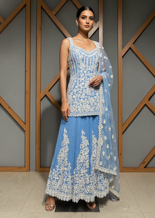 Woman wearing a blue embroidered traditional outfit against a geometric-patterned wall.