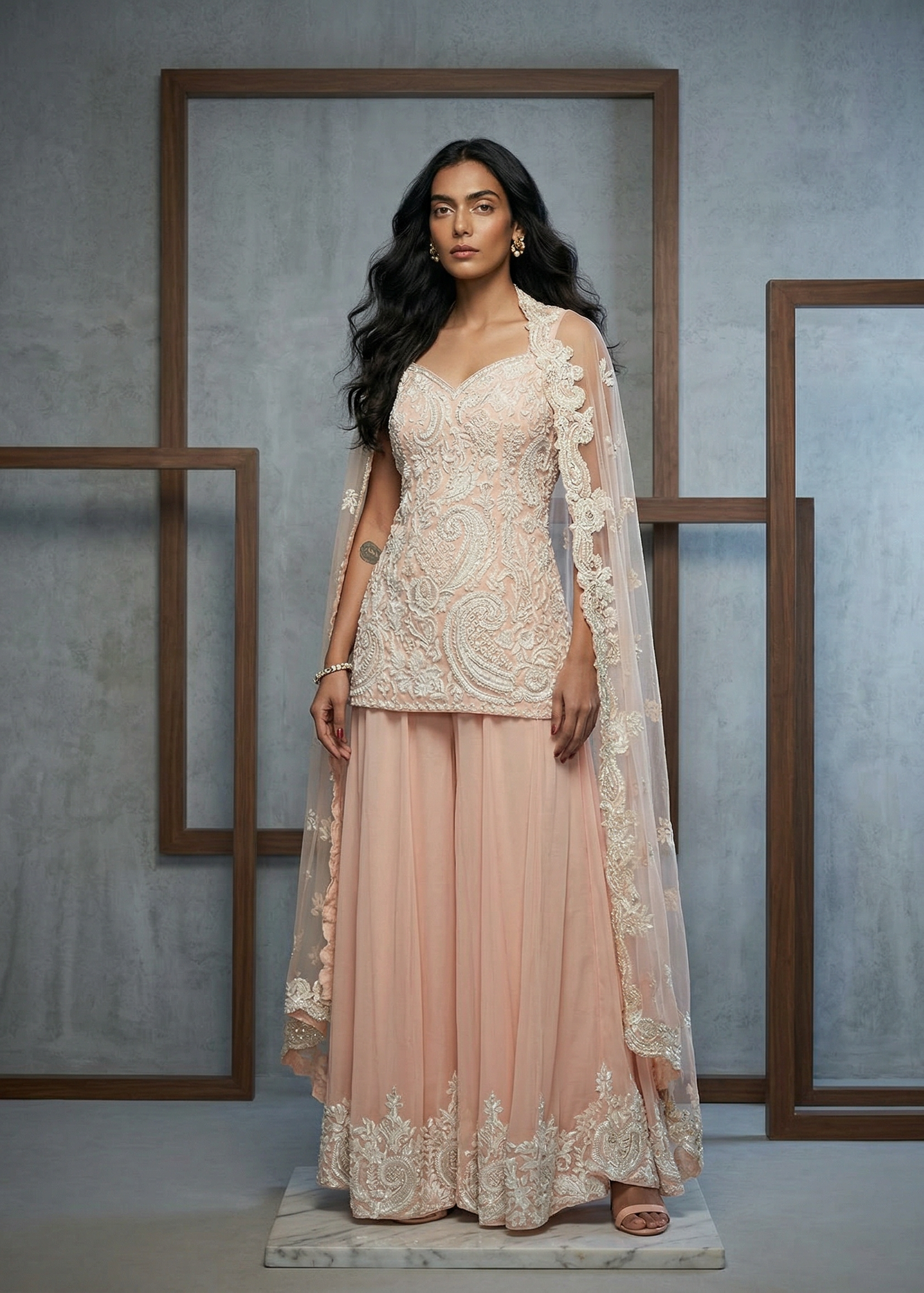 Woman wearing a light pink embroidered outfit with a matching dupatta against a gray background.