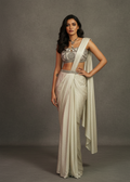 Woman in a saree standing against a plain background