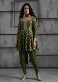 Woman wearing a green traditional outfit with intricate patterns against a gray textured wall.