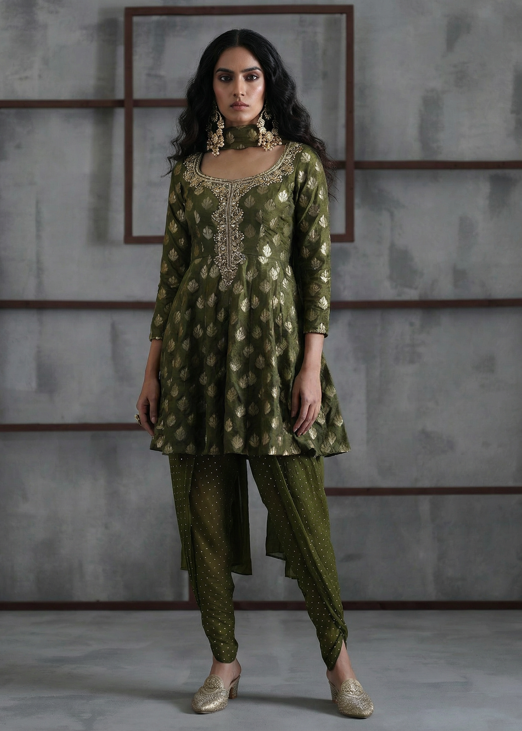 Woman wearing a green traditional outfit with intricate patterns against a gray textured wall.