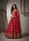 Woman wearing a red traditional outfit with gold patterns in a minimalistic setting.