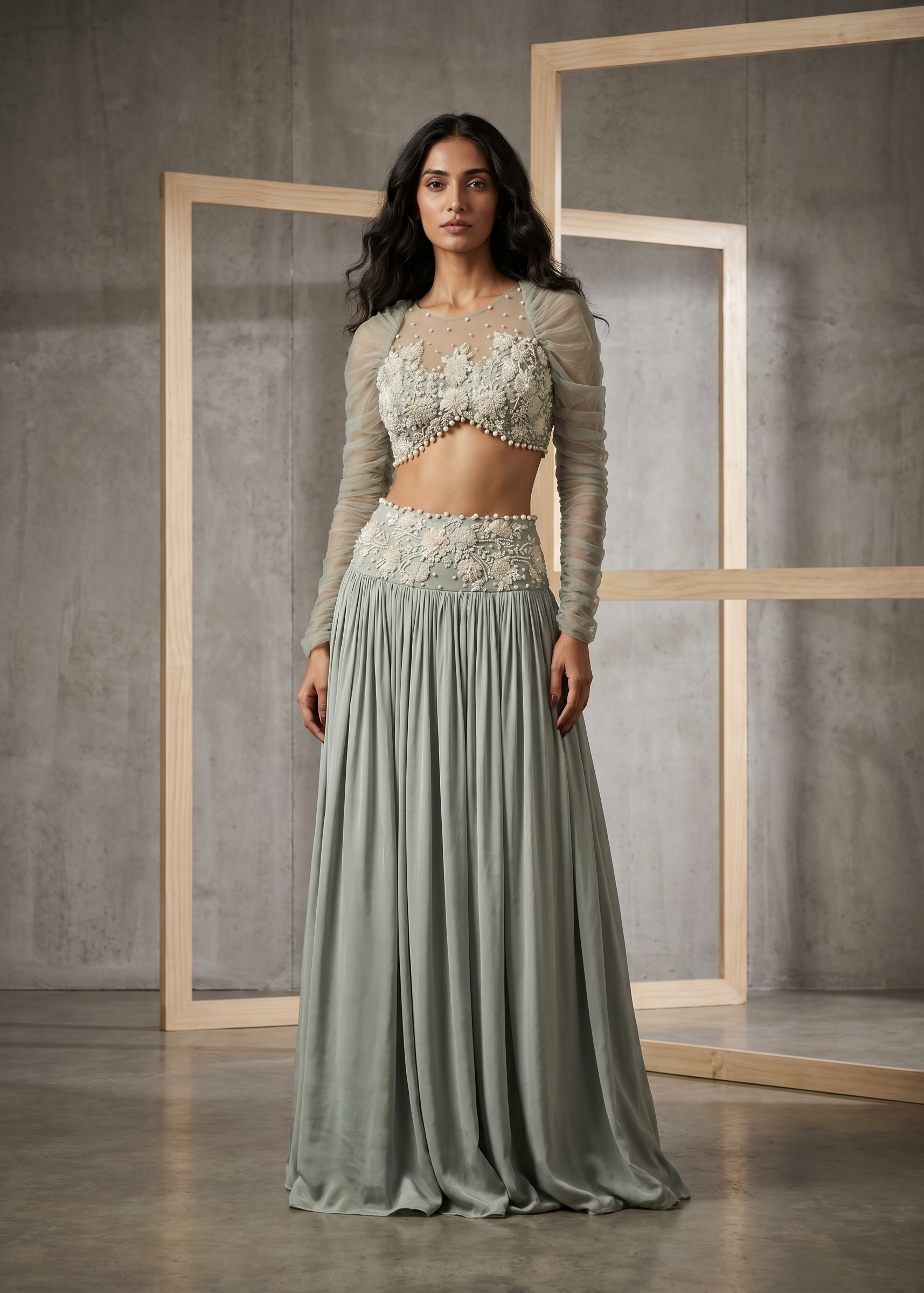 Woman wearing a light green traditional outfit with a textured top and flowing skirt against a gray concrete wall.
