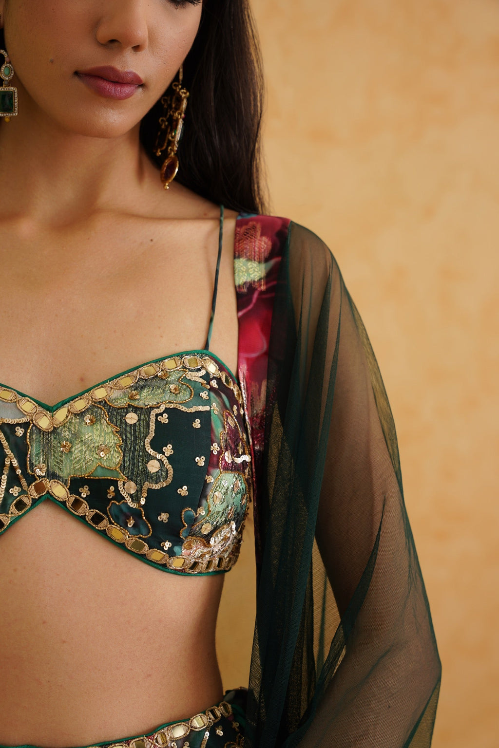 Woman wearing a traditional embroidered blouse with a sheer green and red saree against a beige background