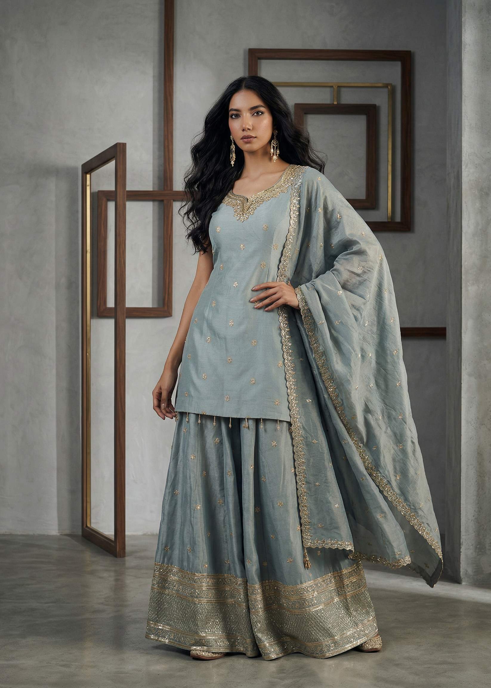 Woman wearing a light blue traditional outfit with gold embroidery in a minimalistic setting.