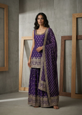Woman wearing a purple traditional outfit with gold patterns in a minimalistic setting.