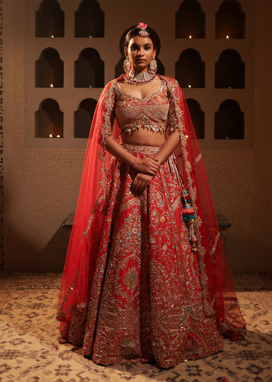 Woman in traditional red and gold embroidered outfit standing in a dimly lit room with arched windows.