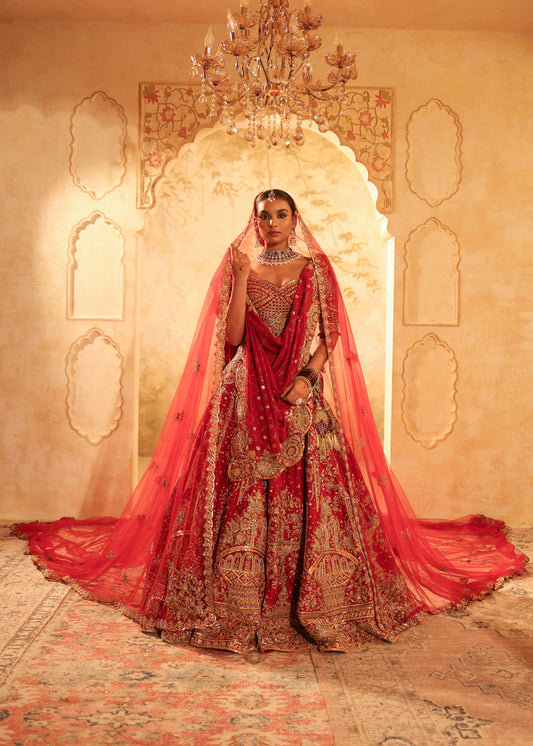 Woman in a red and gold traditional outfit standing in a decorated room with a chandelier.