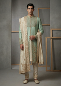 Man wearing a traditional light green sherwani with white embroidery against a gray background