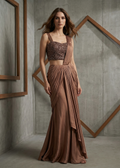 Woman wearing a brown dress standing against a concrete wall with wooden frames.