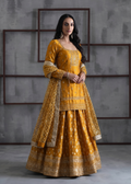 Woman wearing a mustard yellow traditional outfit with intricate patterns against a gray textured wall.