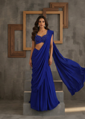 Woman wearing a blue saree with a textured wall and wooden frames in the background