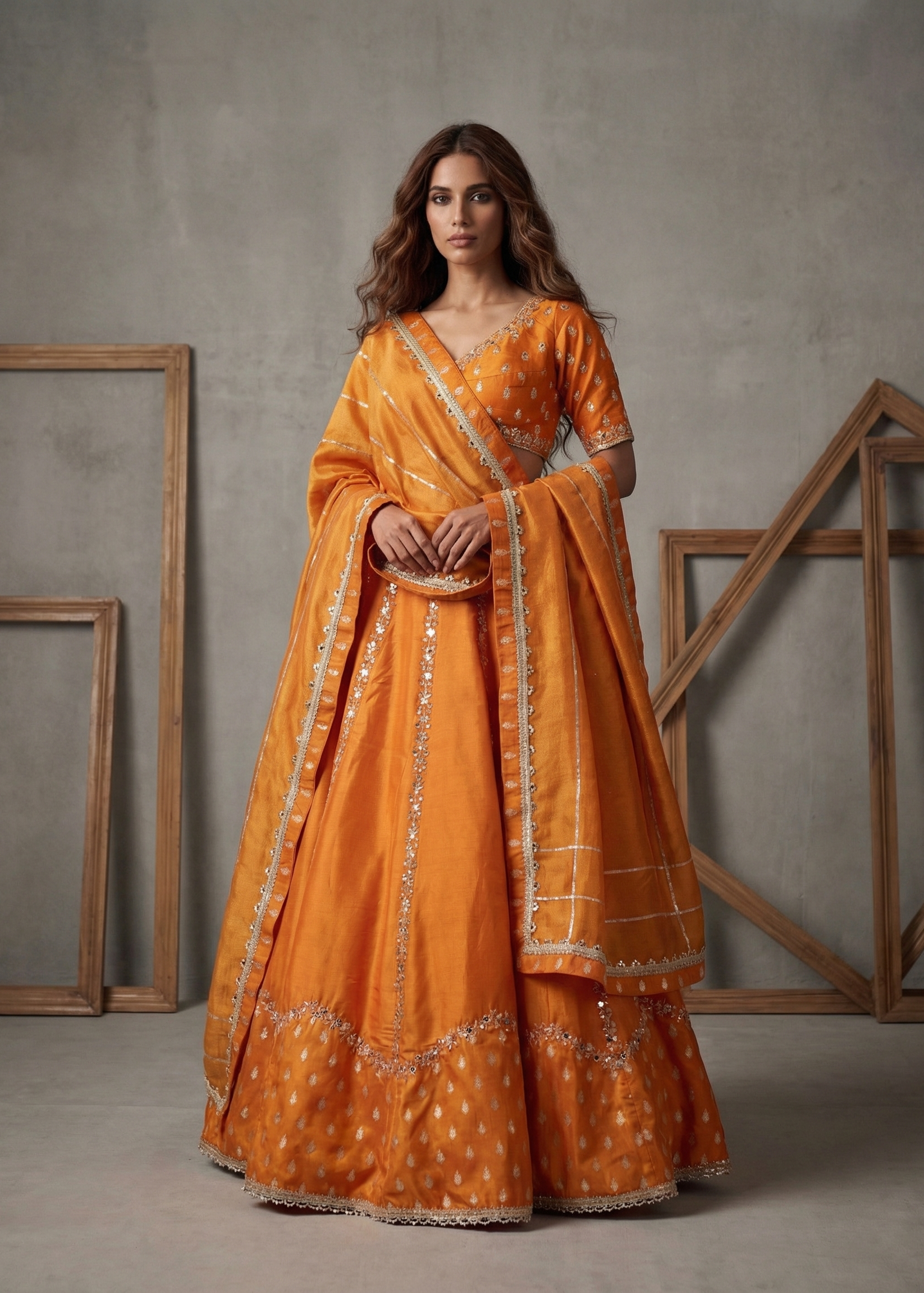 Woman in an orange traditional outfit with a matching dupatta against a gray background