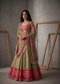 Woman in a traditional outfit with a green and red saree against a gray concrete wall.