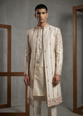 Man wearing a cream embroidered sherwani against a gray background